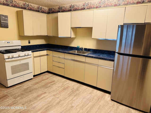 kitchen featuring white range with gas cooktop, a sink, a textured ceiling, dark countertops, and freestanding refrigerator