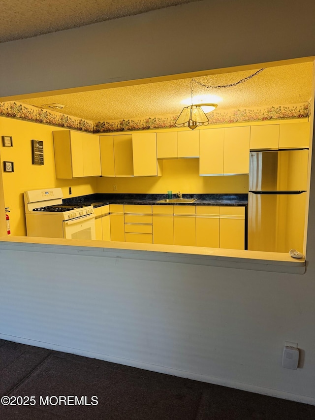 kitchen featuring white gas stove, a sink, dark countertops, a textured ceiling, and freestanding refrigerator