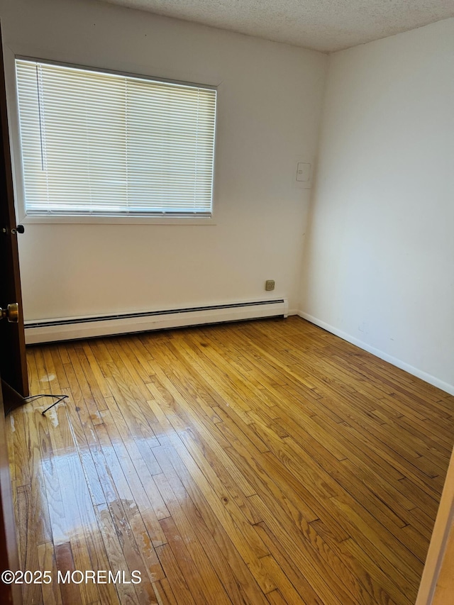 empty room with baseboard heating, a textured ceiling, baseboards, and wood-type flooring