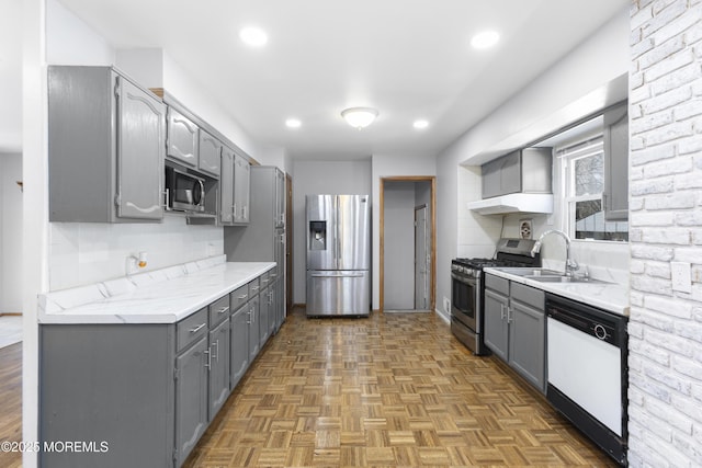 kitchen with gray cabinetry, a sink, tasteful backsplash, appliances with stainless steel finishes, and light countertops