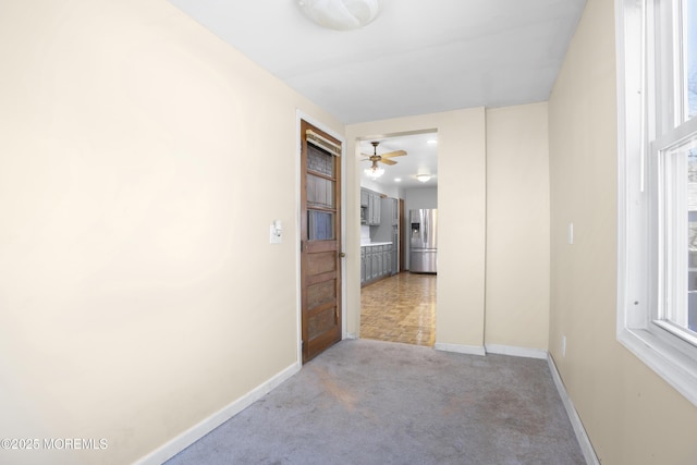 hallway featuring light colored carpet and baseboards