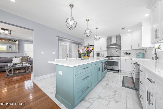 kitchen featuring blue cabinets, marble finish floor, white cabinetry, stainless steel appliances, and wall chimney range hood