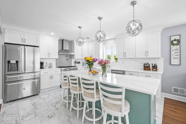 kitchen featuring stainless steel appliances, marble finish floor, wall chimney exhaust hood, and white cabinets