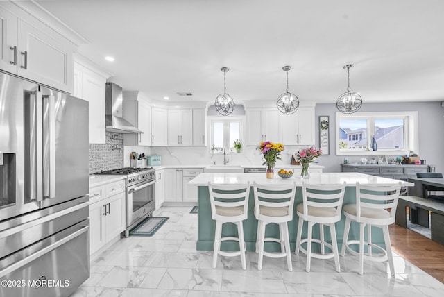 kitchen with light countertops, marble finish floor, stainless steel appliances, wall chimney exhaust hood, and a sink