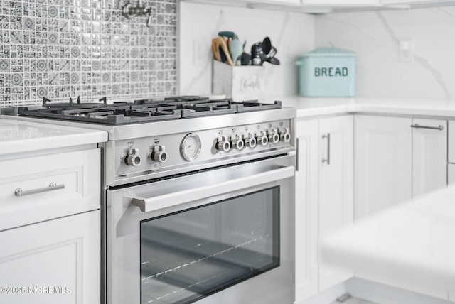 kitchen with tasteful backsplash, white cabinets, stainless steel range, and light countertops