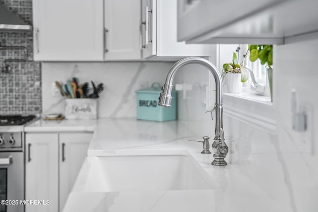 room details with a sink, stainless steel gas stove, tasteful backsplash, and white cabinetry