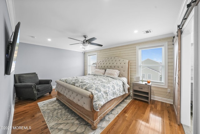 bedroom with baseboards, crown molding, a barn door, and hardwood / wood-style flooring