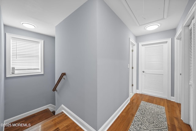 hall featuring attic access, wood finished floors, an upstairs landing, and baseboards