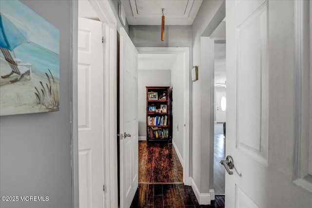 hall with baseboards, attic access, and dark wood-style floors