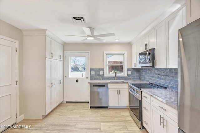 kitchen featuring visible vents, backsplash, stainless steel appliances, white cabinetry, and a sink