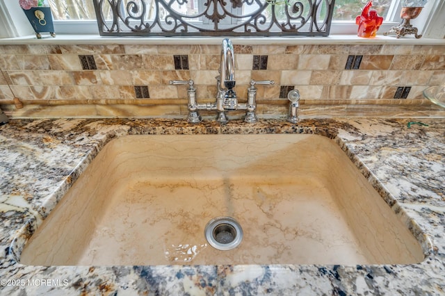 room details featuring a sink, decorative backsplash, and stone counters