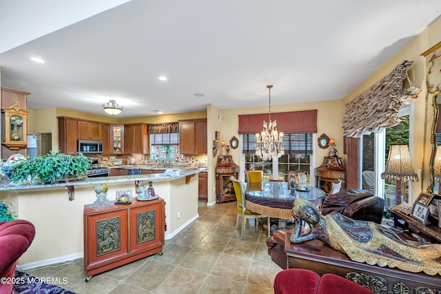 kitchen with an inviting chandelier, a peninsula, decorative backsplash, appliances with stainless steel finishes, and brown cabinets