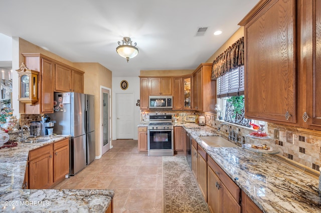 kitchen featuring tasteful backsplash, visible vents, light stone counters, appliances with stainless steel finishes, and brown cabinetry