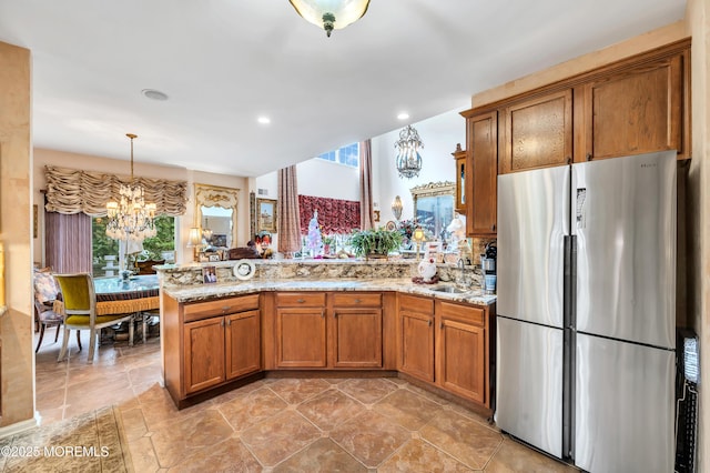 kitchen featuring an inviting chandelier, a peninsula, brown cabinetry, and freestanding refrigerator