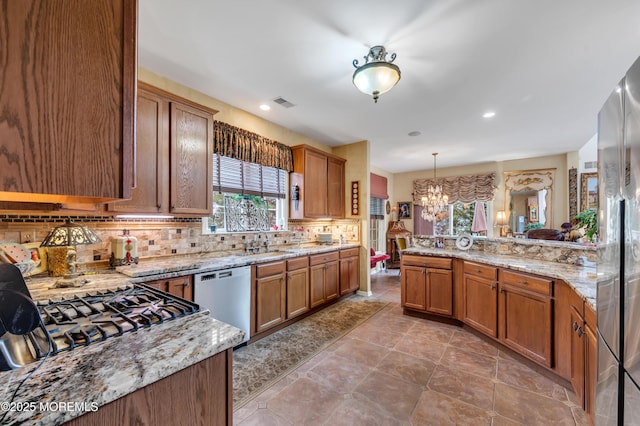 kitchen with decorative backsplash, brown cabinets, appliances with stainless steel finishes, and an inviting chandelier