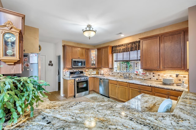 kitchen featuring brown cabinets, light stone counters, a sink, appliances with stainless steel finishes, and decorative backsplash