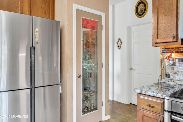 kitchen with light stone counters, brown cabinetry, appliances with stainless steel finishes, tile patterned floors, and backsplash