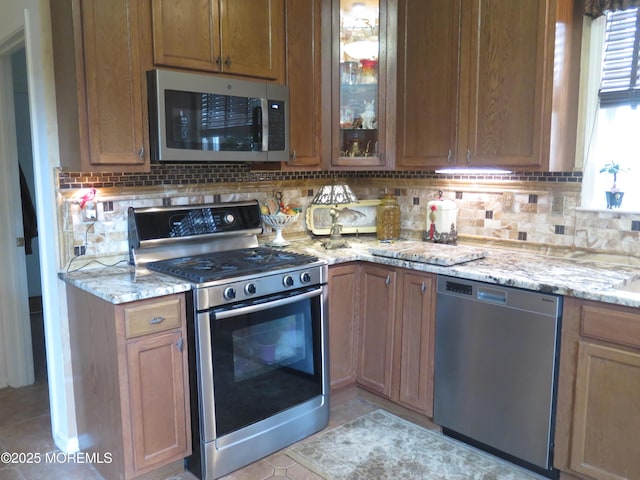 kitchen featuring decorative backsplash, light tile patterned floors, light stone countertops, and stainless steel appliances