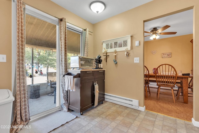 interior space with baseboard heating, dark brown cabinets, a ceiling fan, and baseboards