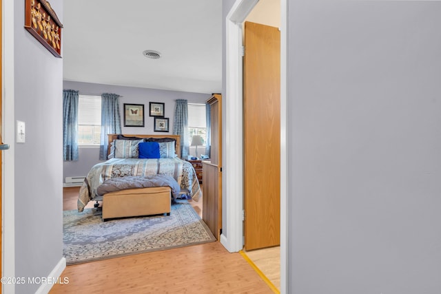 bedroom with visible vents, baseboards, baseboard heating, and wood finished floors