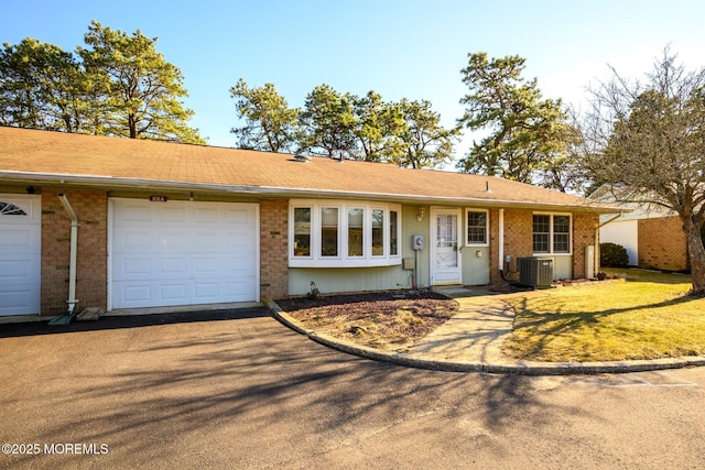 ranch-style house with driveway, brick siding, central AC, and an attached garage