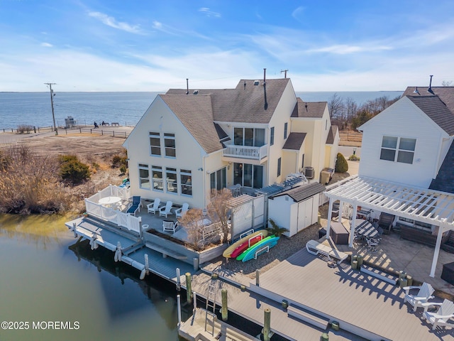 rear view of house with a balcony, roof with shingles, a patio, and a water view