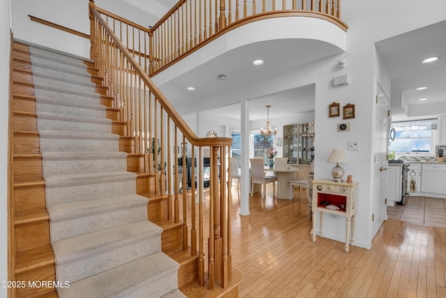 staircase with hardwood / wood-style floors, a towering ceiling, a wealth of natural light, and a chandelier