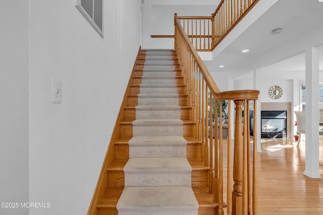 stairs featuring visible vents, wood finished floors, recessed lighting, a multi sided fireplace, and a towering ceiling