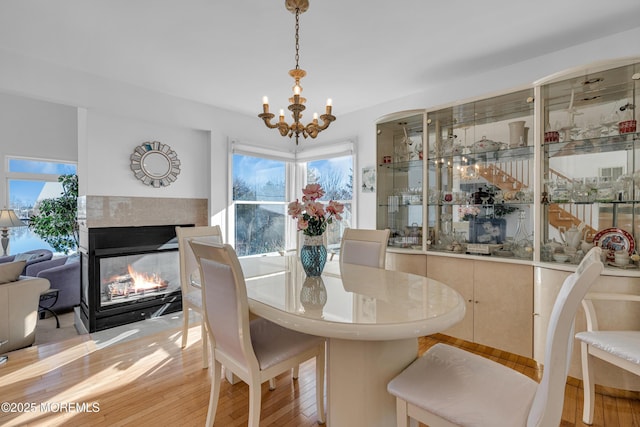 dining space with a multi sided fireplace, a notable chandelier, and wood finished floors