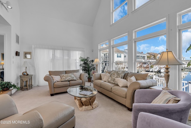 living room featuring a wealth of natural light, visible vents, carpet flooring, and a towering ceiling