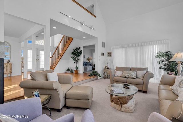 living room featuring visible vents, a glass covered fireplace, wood finished floors, a towering ceiling, and stairs