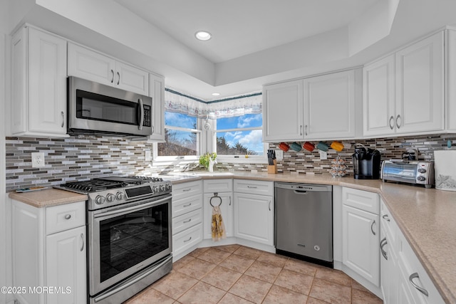 kitchen featuring tasteful backsplash, white cabinets, stainless steel appliances, and light countertops