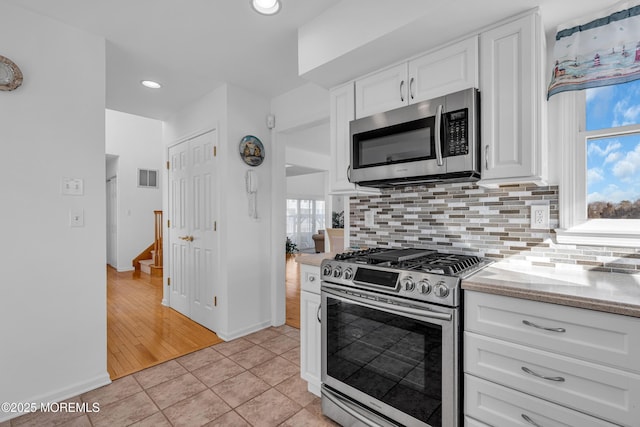 kitchen with visible vents, white cabinetry, stainless steel appliances, light tile patterned floors, and decorative backsplash