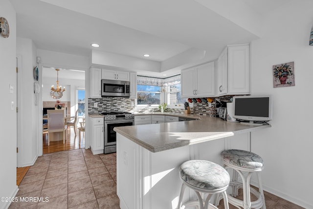 kitchen with decorative backsplash, white cabinets, a peninsula, and stainless steel appliances