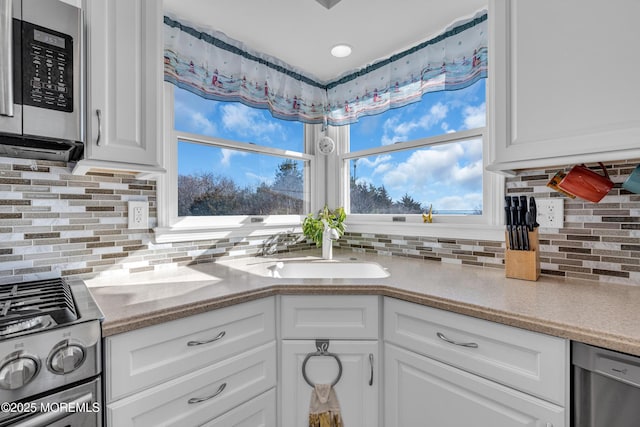 kitchen with a sink, white cabinets, backsplash, and stainless steel appliances