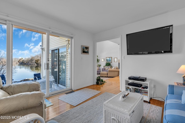 living area with visible vents, wood finished floors, a water view, and baseboards