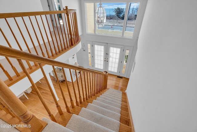 stairs featuring visible vents, wood finished floors, french doors, a high ceiling, and a chandelier