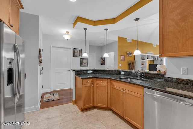 kitchen with a sink, brown cabinets, appliances with stainless steel finishes, and dark stone countertops