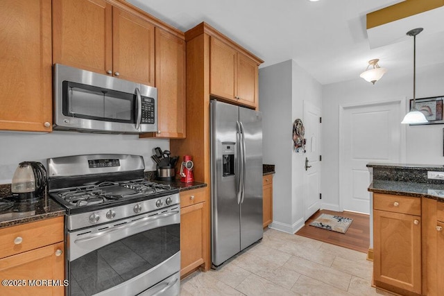 kitchen featuring dark stone countertops, stainless steel appliances, brown cabinets, and decorative light fixtures