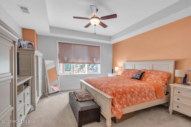 bedroom with visible vents, baseboards, light colored carpet, a tray ceiling, and a ceiling fan