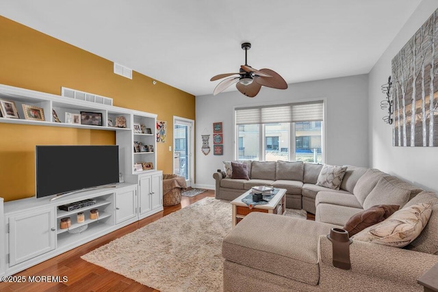 living room with ceiling fan, visible vents, baseboards, and wood finished floors