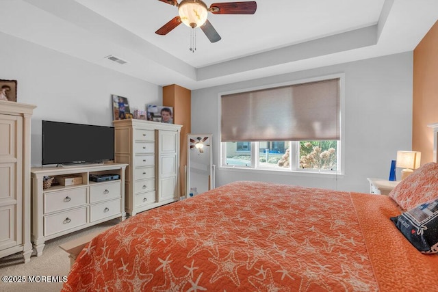 carpeted bedroom with visible vents, a raised ceiling, and a ceiling fan