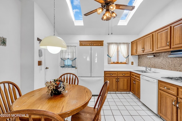 kitchen featuring range hood, white appliances, brown cabinetry, a sink, and lofted ceiling with skylight