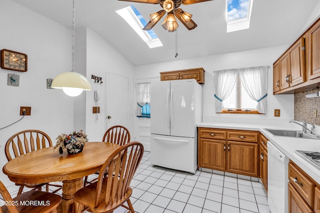 kitchen with lofted ceiling with skylight, a sink, white appliances, brown cabinetry, and light tile patterned floors