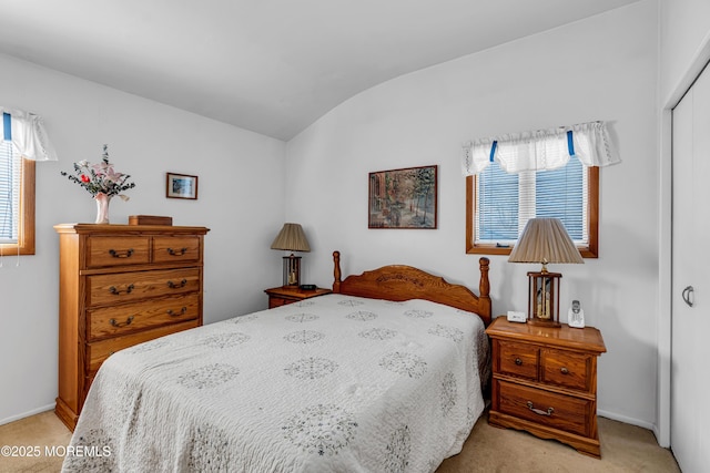 bedroom featuring lofted ceiling, baseboards, a closet, and light carpet