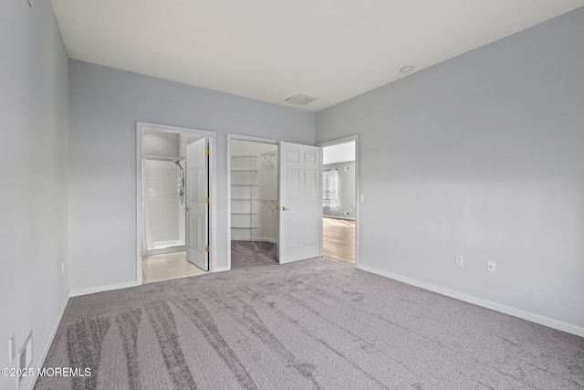 unfurnished bedroom with a closet, connected bathroom, carpet flooring, baseboards, and a spacious closet