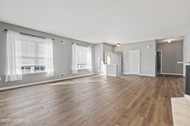 unfurnished living room featuring visible vents, baseboards, and wood finished floors