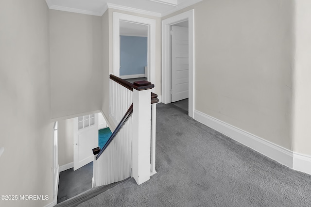 hallway with an upstairs landing, ornamental molding, baseboards, and dark colored carpet