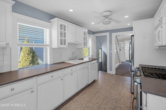 kitchen with a sink, white appliances, dark countertops, and tasteful backsplash