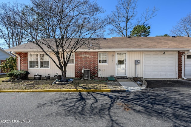 ranch-style house featuring aphalt driveway, an attached garage, cooling unit, and brick siding